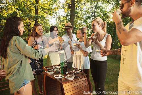 Image of Happy friends eating and drinking beers at barbecue dinner on sunset time