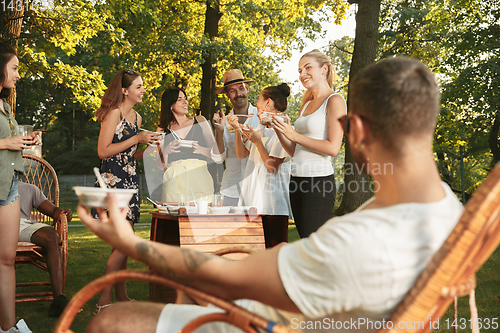 Image of Happy friends eating and drinking beers at barbecue dinner on sunset time