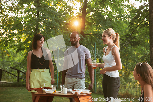 Image of Happy friends eating and drinking beers at barbecue dinner on sunset time