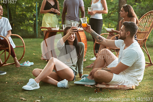 Image of Happy friends eating and drinking beers at barbecue dinner on sunset time