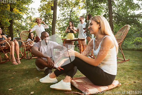 Image of Happy friends eating and drinking beers at barbecue dinner on sunset time