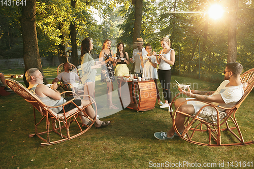 Image of Happy friends eating and drinking beers at barbecue dinner on sunset time