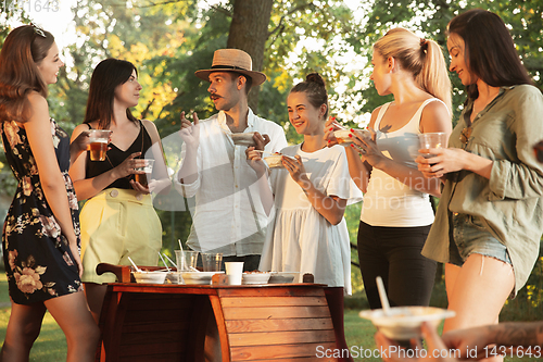 Image of Happy friends eating and drinking beers at barbecue dinner on sunset time