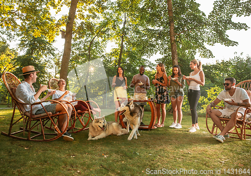 Image of Happy friends eating and drinking beers at barbecue dinner on sunset time