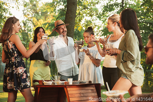 Image of Happy friends eating and drinking beers at barbecue dinner on sunset time