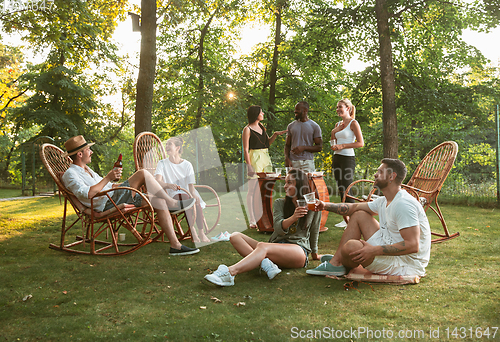 Image of Happy friends eating and drinking beers at barbecue dinner on sunset time