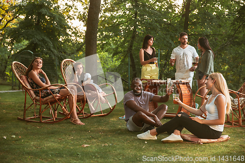 Image of Happy friends eating and drinking beers at barbecue dinner on sunset time