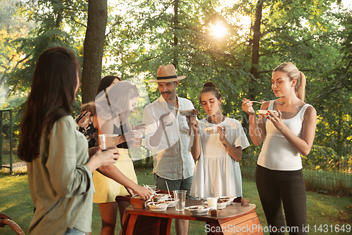 Image of Happy friends eating and drinking beers at barbecue dinner on sunset time