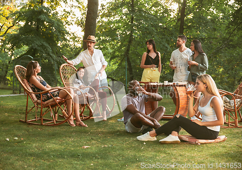 Image of Happy friends eating and drinking beers at barbecue dinner on sunset time