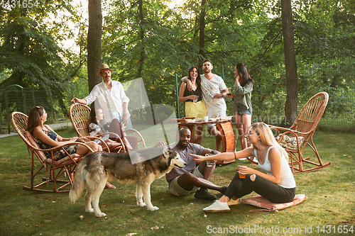 Image of Happy friends eating and drinking beers at barbecue dinner on sunset time