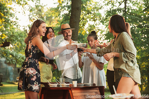 Image of Happy friends eating and drinking beers at barbecue dinner on sunset time