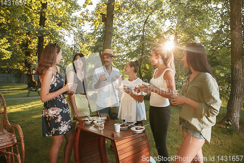 Image of Happy friends eating and drinking beers at barbecue dinner on sunset time