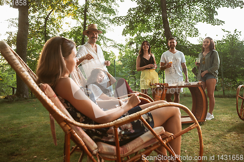 Image of Happy friends eating and drinking beers at barbecue dinner on sunset time