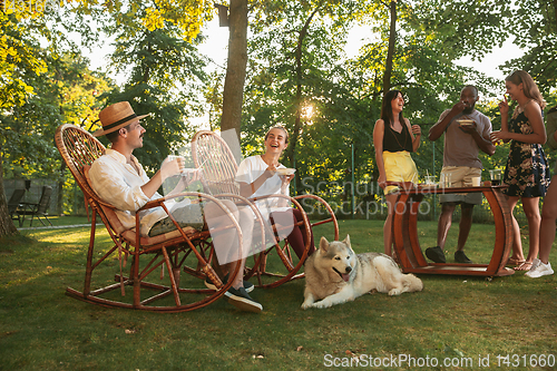 Image of Happy friends eating and drinking beers at barbecue dinner on sunset time