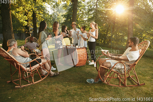 Image of Happy friends eating and drinking beers at barbecue dinner on sunset time