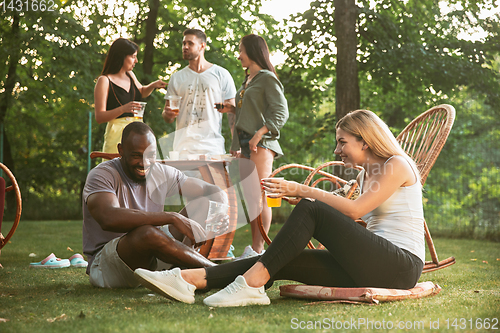 Image of Happy friends eating and drinking beers at barbecue dinner on sunset time