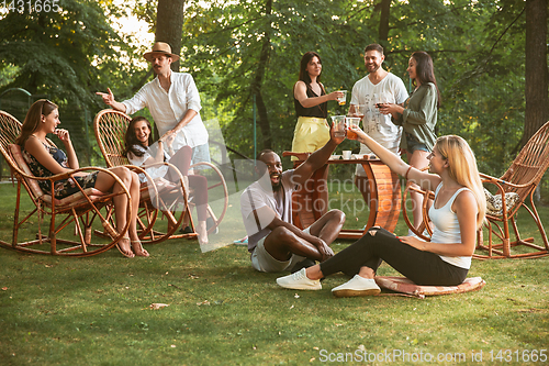 Image of Happy friends eating and drinking beers at barbecue dinner on sunset time