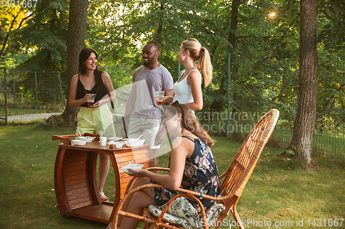 Image of Happy friends eating and drinking beers at barbecue dinner on sunset time