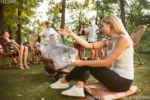 Image of Happy friends eating and drinking beers at barbecue dinner on sunset time