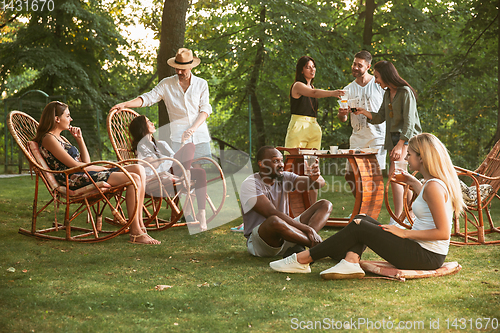 Image of Happy friends eating and drinking beers at barbecue dinner on sunset time