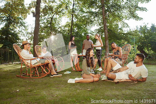 Image of Happy friends eating and drinking beers at barbecue dinner on sunset time