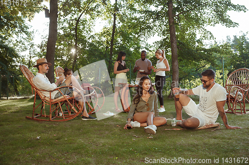 Image of Happy friends eating and drinking beers at barbecue dinner on sunset time