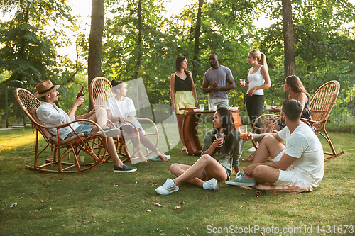 Image of Happy friends eating and drinking beers at barbecue dinner on sunset time