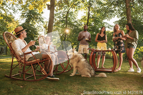 Image of Happy friends eating and drinking beers at barbecue dinner on sunset time