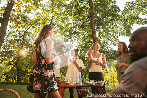 Image of Happy friends eating and drinking beers at barbecue dinner on sunset time