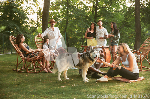 Image of Happy friends eating and drinking beers at barbecue dinner on sunset time