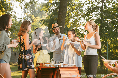 Image of Happy friends eating and drinking beers at barbecue dinner on sunset time