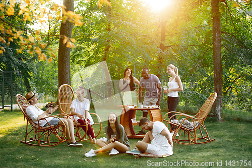 Image of Happy friends eating and drinking beers at barbecue dinner on sunset time