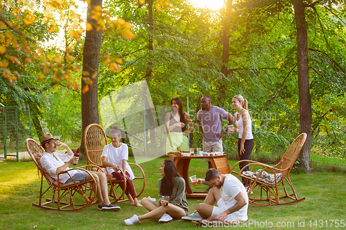 Image of Happy friends eating and drinking beers at barbecue dinner on sunset time