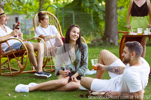 Image of Happy friends eating and drinking beers at barbecue dinner on sunset time