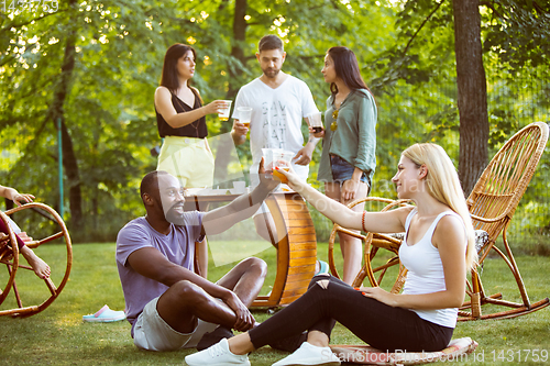 Image of Happy friends eating and drinking beers at barbecue dinner on sunset time