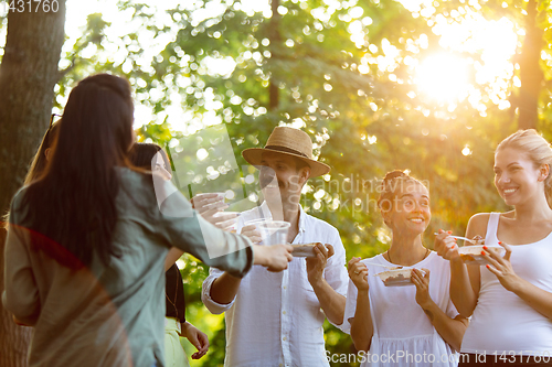 Image of Happy friends eating and drinking beers at barbecue dinner on sunset time