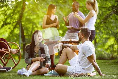 Image of Happy friends eating and drinking beers at barbecue dinner on sunset time