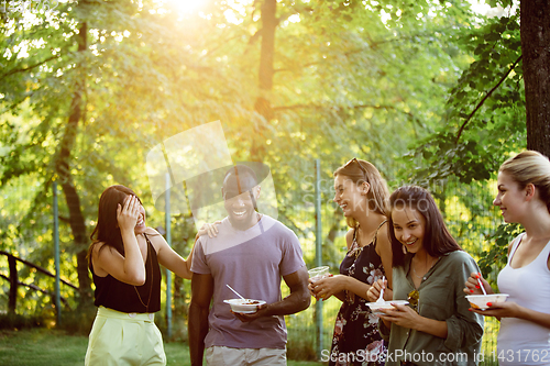 Image of Happy friends eating and drinking beers at barbecue dinner on sunset time