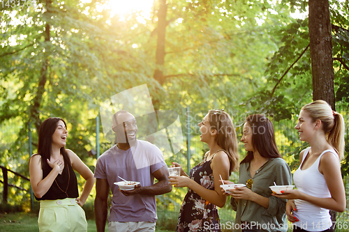 Image of Happy friends eating and drinking beers at barbecue dinner on sunset time