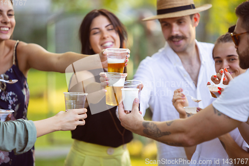 Image of Happy friends eating and drinking beers at barbecue dinner on sunset time