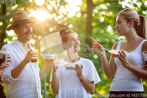 Image of Happy friends eating at barbecue dinner on sunset time