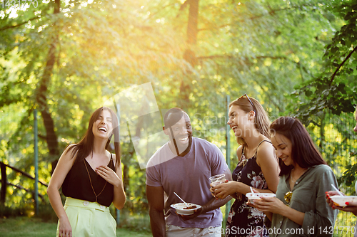 Image of Happy friends eating and drinking beers at barbecue dinner on sunset time