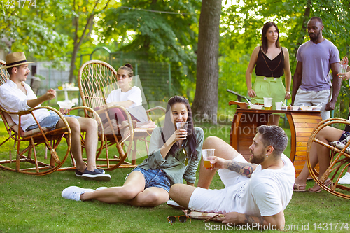 Image of Happy friends eating and drinking beers at barbecue dinner on sunset time