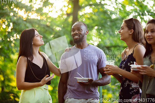 Image of Happy friends eating and drinking beers at barbecue dinner on sunset time