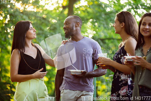 Image of Happy friends eating and drinking beers at barbecue dinner on sunset time