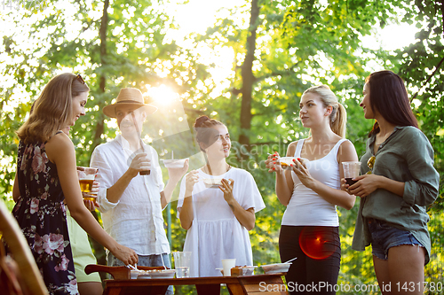 Image of Happy friends eating and drinking beers at barbecue dinner on sunset time