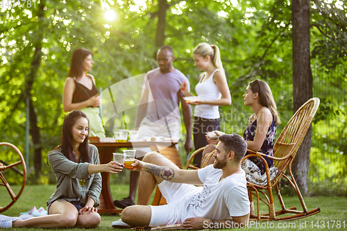 Image of Happy friends eating and drinking beers at barbecue dinner on sunset time