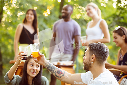 Image of Happy friends eating and drinking beers at barbecue dinner on sunset time