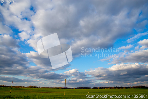 Image of Landscape with blue cloudy sky, cereal field and trees.