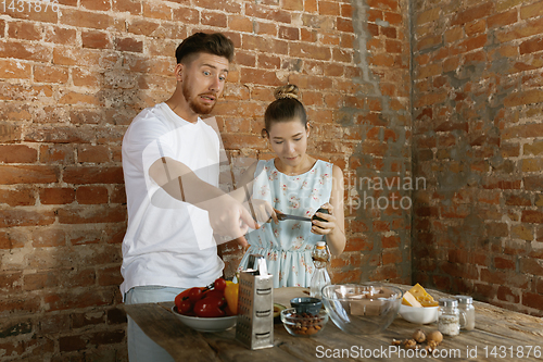 Image of Young caucasian couple cooking together against brick wall
